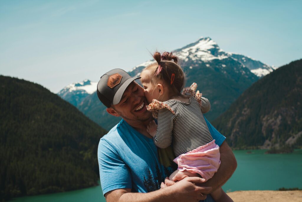 Tender moment of a father and daughter hugging in a scenic mountain setting.