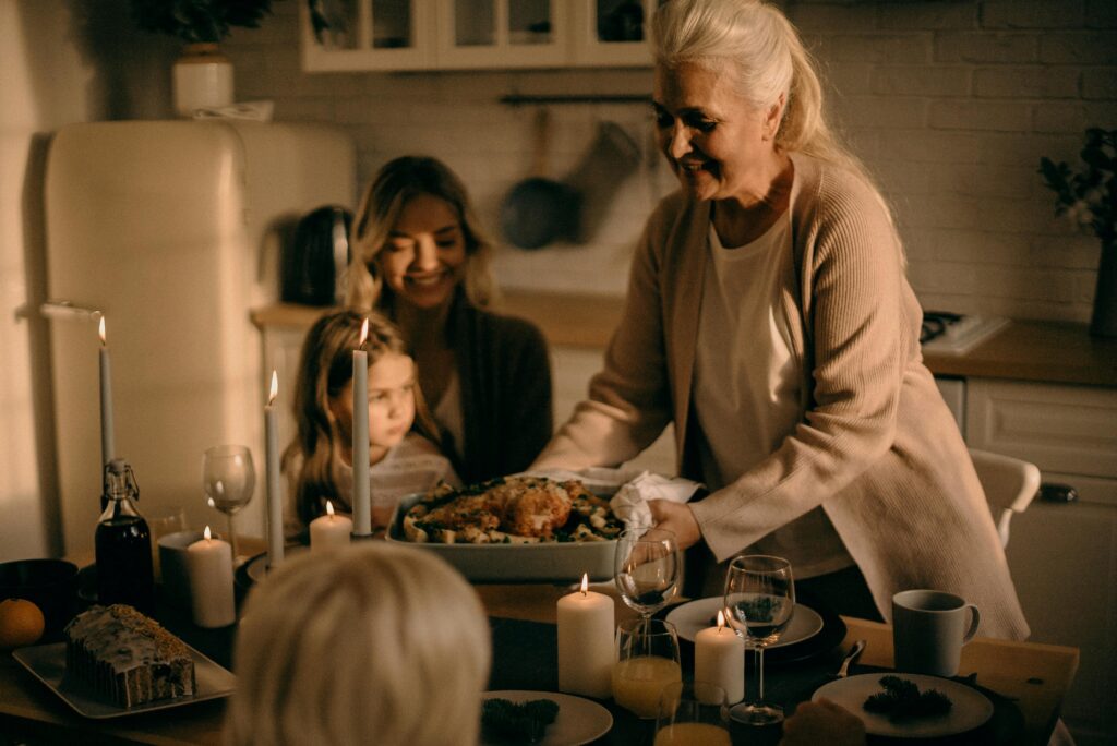 A grandmother serves a festive turkey dinner to family gathered around a warmly lit table.